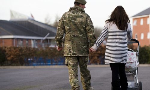 Male soldier holding hands with woman pushing pram