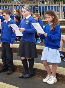 schoolchildren reading aloud at an outdoor assembly