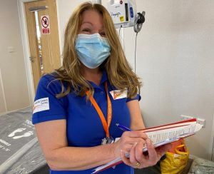 Blonde woman in mask and blue shirt with clipboard