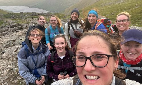 Smiling team of climbers on Scafell Pike, mountains and lake behind them