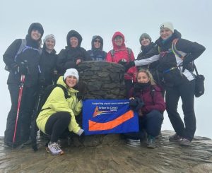 Team of climbers holding up action for carers flag on top of mount snowden in the fog