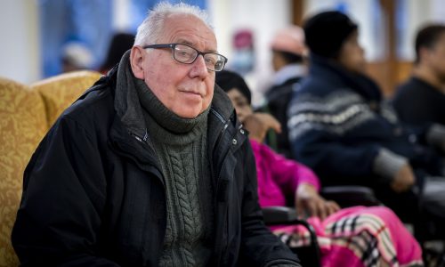 Older male carer with jacket on looks into camera thoughtfully