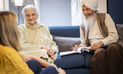 Sikh couple talk to a researcher sat on sofa smiling