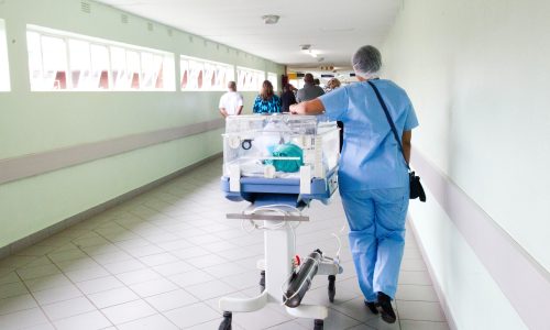 Hospital staff wheels a trolley down a hospital corridor.
