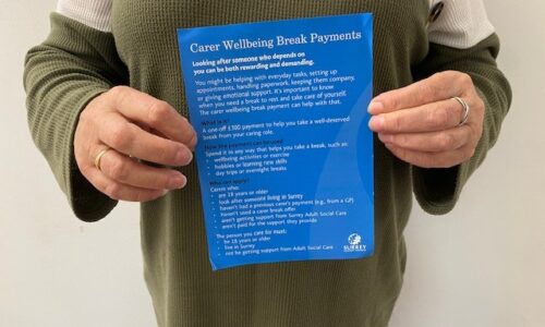 Person holds the blue leaflet with information on Surrey's wellbeing break payments for carers