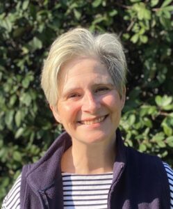 Julie Law Action for Carers Hospital Adviser standing outside against a green background smiling