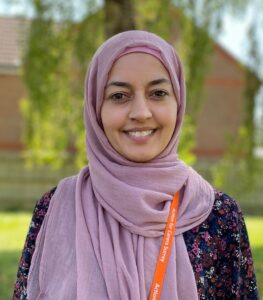 Action for Carers Hospital Adviser Naheeda Majid standing outside against green background smiling